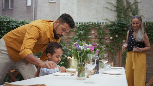 Young father with small son and his grandmother setting table for family dinner outdoors in back yard.