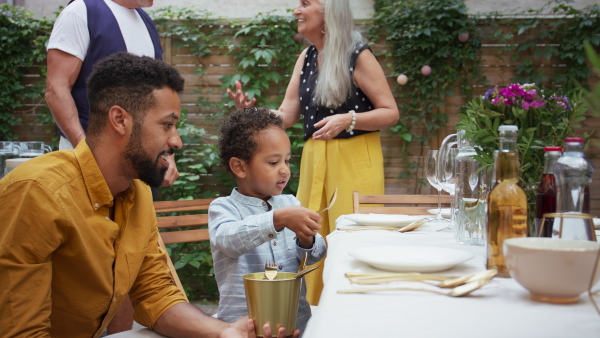 A young African American father with small son setting table for family dinner outdoors in back yard.