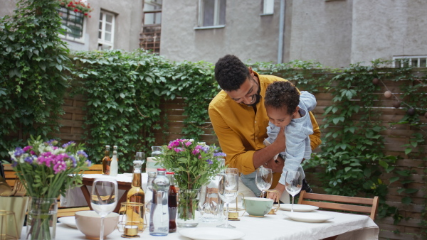 A father with small son and his grandparents setting table for family dinner outdoors in back yard.