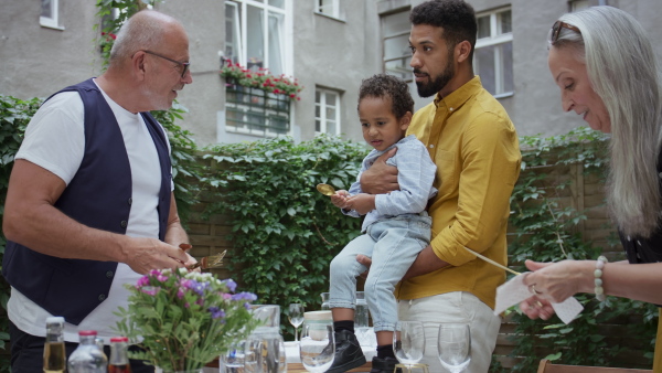 A little boy with his father and grandparents setting table for family dinner outdoors in back yard.