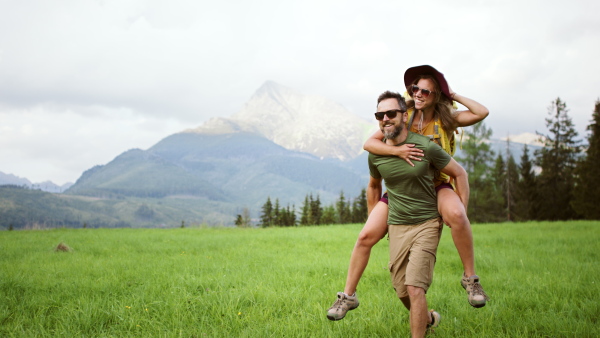 A young man giving piggyback ride to woman while hiking through mountains.