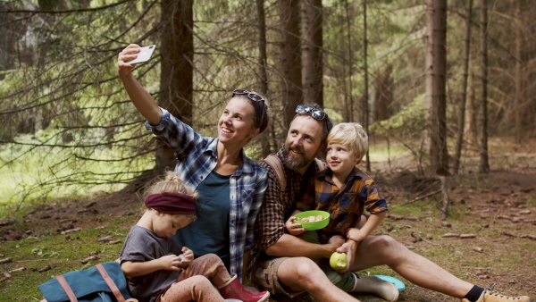 A family with small children having picnic in summer forest and taking selfie.