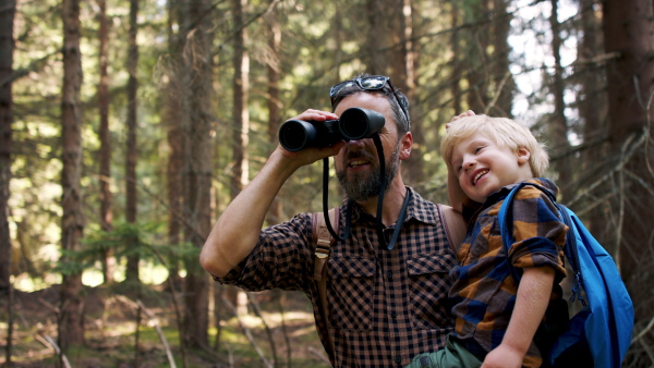 A father with small son looking through binoculars in summer forest.