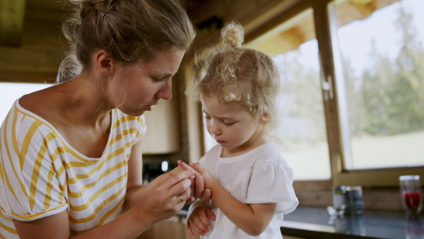 A mother blowing her little daughter's bleeding finger cut with knife at home.