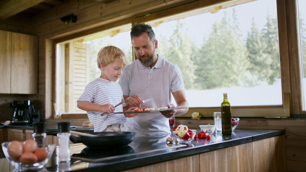 A father with small son cooking together in kitchen, holiday in private apartment.