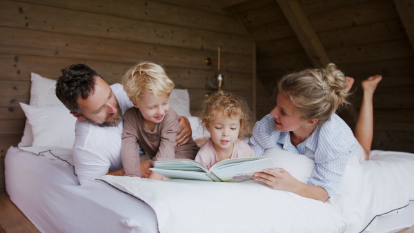 A happy young family with small children having fun in bed when reading book.