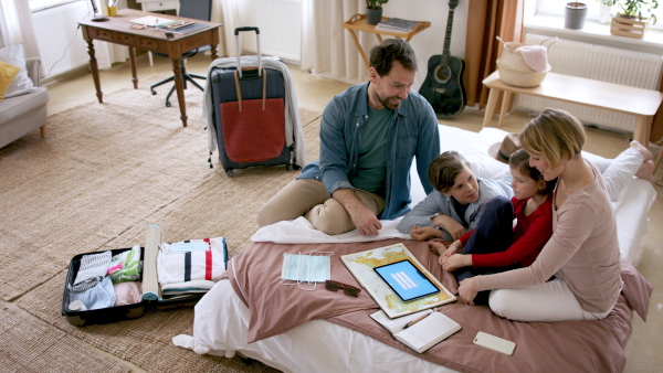 Top view of beautiful family packing and making preparations for vacation on tablet.