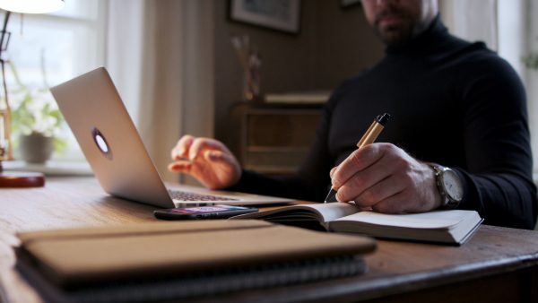 Handsome man working on laptop and making notes at home office.