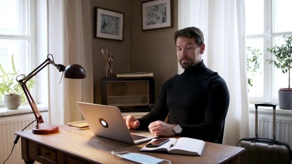 Handsome man working on laptop at home office, looking at camera.