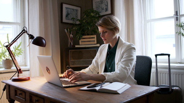 Beautiful woman working on laptop at home office and looking at camera.