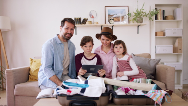 A beautiful family packing, making preparations for vacation on tablet and looking at camera.