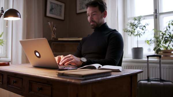 Handsome man working on laptop at home office and making notes.