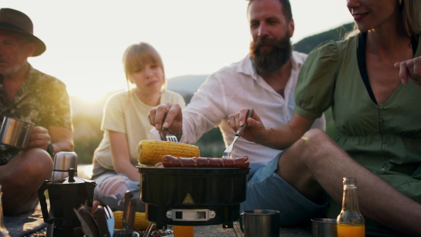 A happy multigeneration family on summer holiday trip, barbecue by lake.