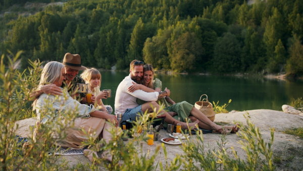 A happy multigeneration family on summer holiday trip, barbecue by lake.