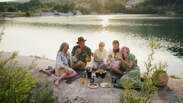 A happy multigeneration family on summer holiday trip, barbecue by lake.