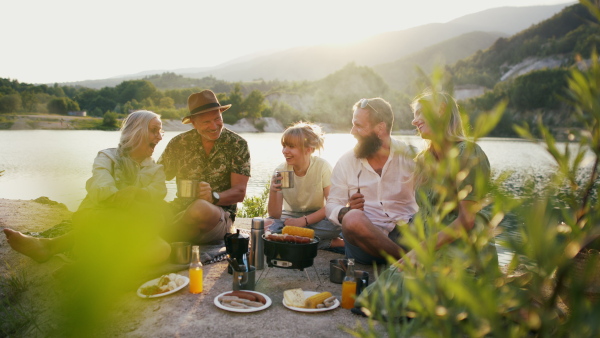 A happy multigeneration family on summer holiday trip, barbecue by lake.