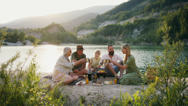 A happy multigeneration family on summer holiday trip, barbecue by lake.