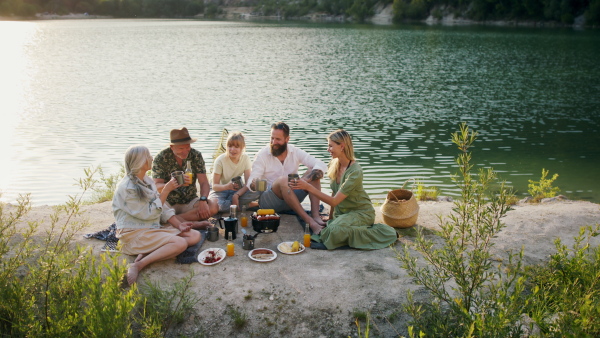 A happy multigeneration family on summer holiday trip, barbecue by lake.