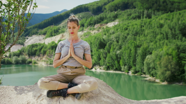 A mid adult woman tourist on hiking trip on summer holiday, doing yoga and meditating.