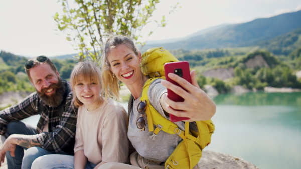 A happy family with preteen daughter on hiking trip on summer holiday, resting and taking selfie