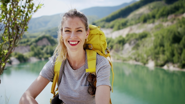 A happy mid adult woman tourist with smartphone hiking in nature by lake.