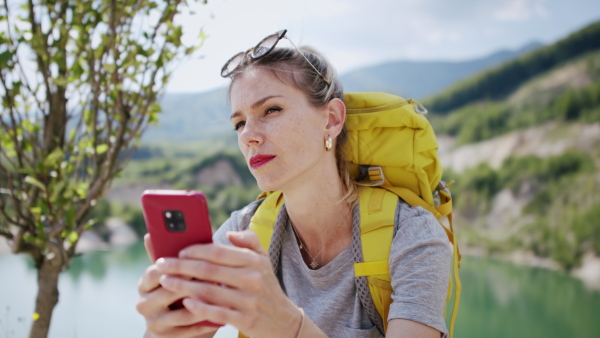 A happy mid adult woman tourist with smartphone hiking in nature by lake.