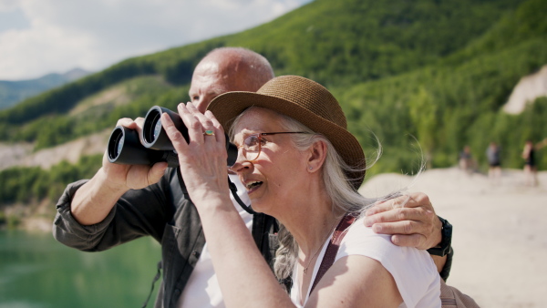 A happy senior couple on hiking trip on summer holiday, using binoculars.