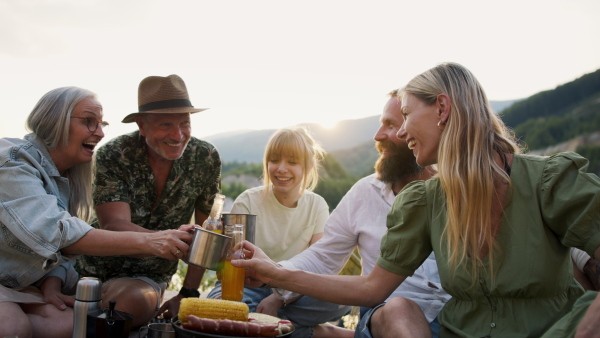 A happy multigeneration family on summer holiday trip, barbecue by lake.