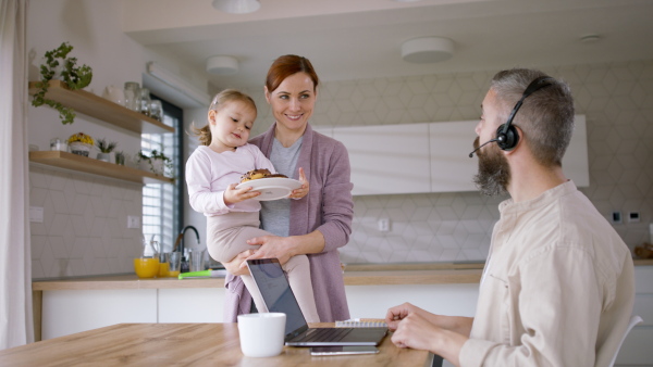 A beautiful family at home, father working on laptop, getting breakfast.