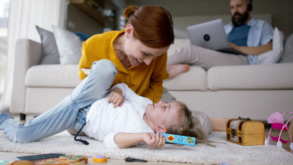 A beautiful family at home, father working, mother playing with daughter.