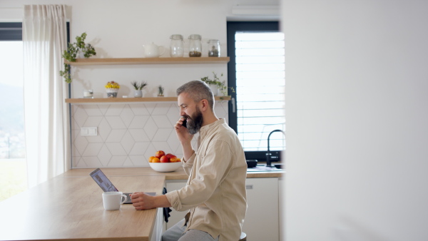 A side view of hipster businessman at home office, having a call and coffee.