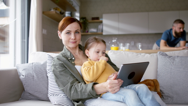 A beautiful family at home, father working, mother with daughter playing with tablet and looking at camera.