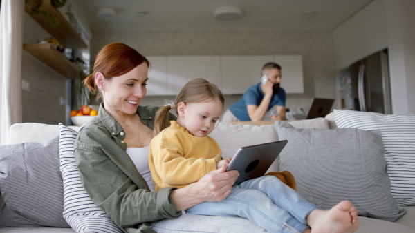 A happy family at home, father working, mother with daughter playing with tablet.