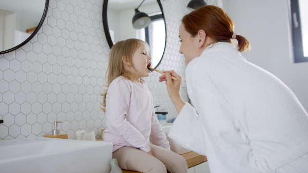 Busy mother in bathrobe tooth brushing daughters teeth in the morning.