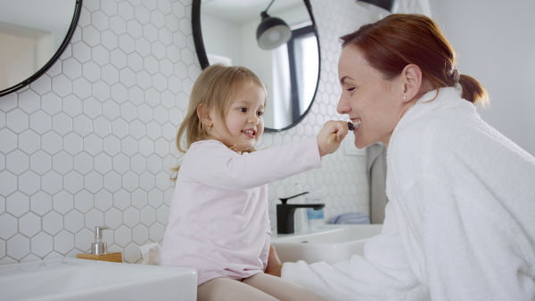 Small daughter tooth brushing mothers teeth in the morning.