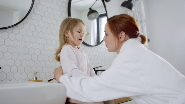 Busy mother in bathrobe tooth brushing daughters teeth and hugging her in the morning..