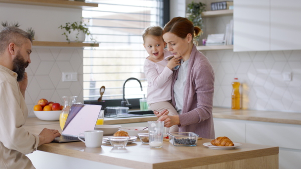 A happy family at home, mother preparing a breakfast, father working. Home office concept.