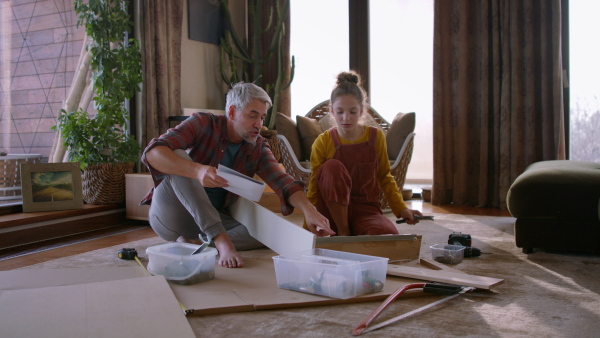 A father and teen daughter assembling new furniture in the renovated apartment