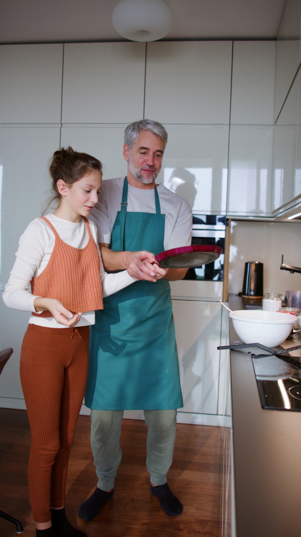 A vertical footage of eenage daughter with her father cooking in kitchen together.