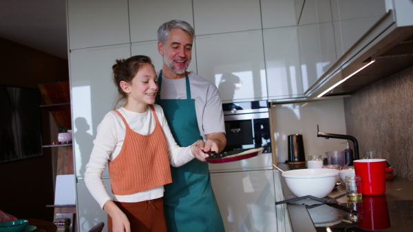 A teenage daughter with her father cooking in kitchen together.