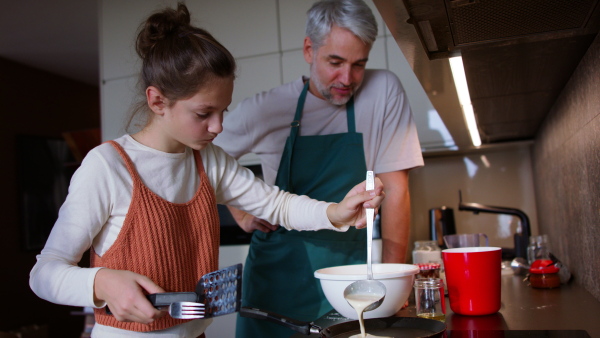 A teenage daughter with her father cooking in kitchen together.