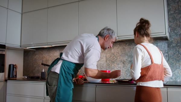 A teenage daughter with her father cooking in kitchen together.