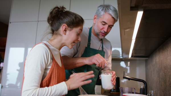 A teenage daughter with her father cooking in kitchen together.