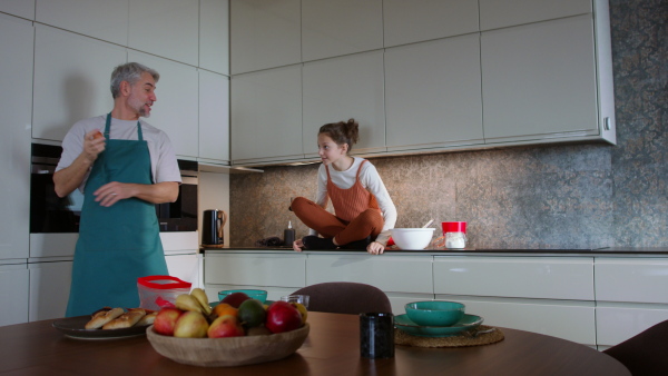 A teenage daughter with her father cooking in kitchen together.