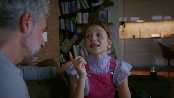 A sad teenage girl crying when talking to her father at home.