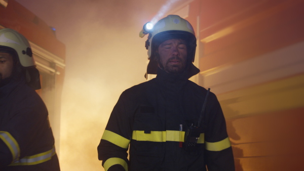 A mid adult firefighter man at action looking at camera with fire truck in background at night.