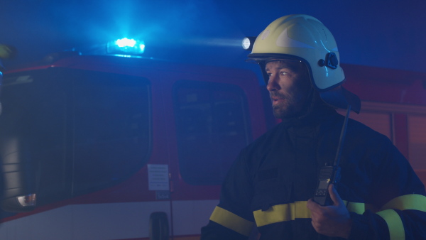 A mature firefighter chief giving instructions to crew at action with fire truck at background at night.