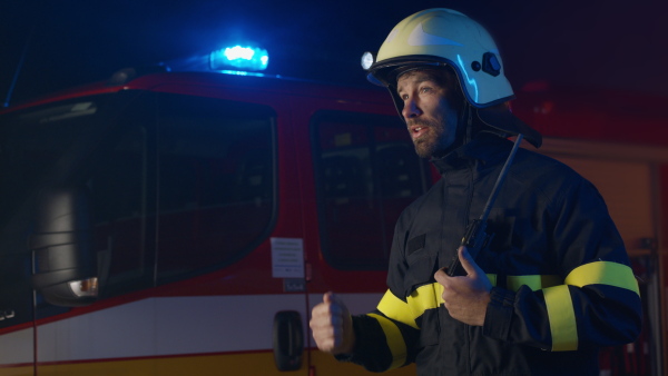 A mature firefighter chief giving instructions to crew at action with fire truck at background at night.