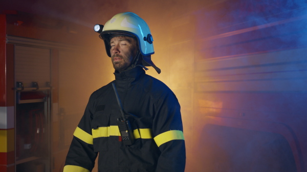 A mid adult dirty male firefighter looking at camera with fire truck at background at night.