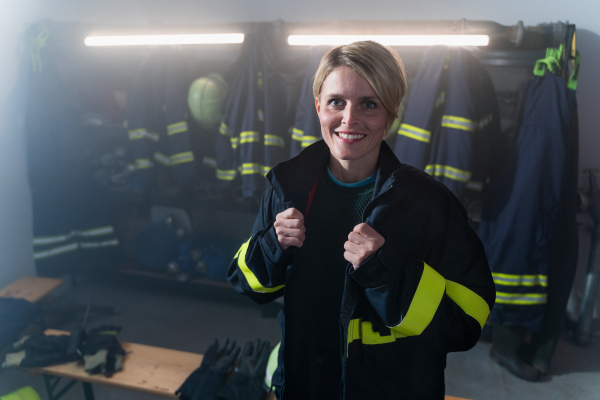 A mid adult female firefighter looking at camera indoors in fire station at night.